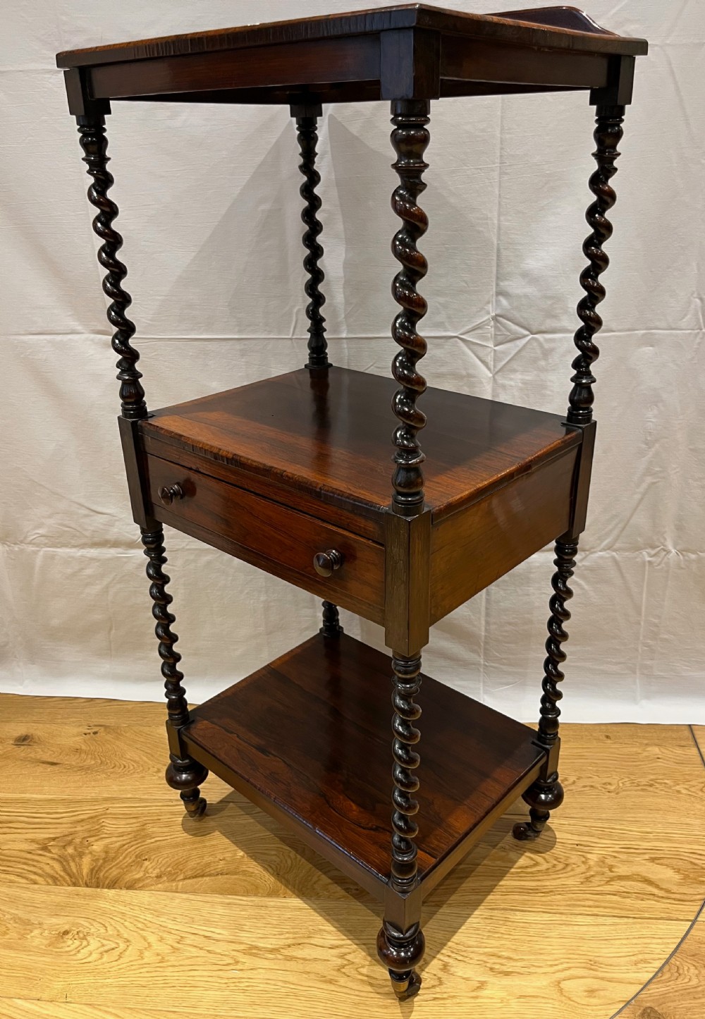 A mid-Victorian dark rosewood whatnot etagere featuring three open tiers, barley twist pillar supports, a central drawer, a gallery back, and turned feet. View VII