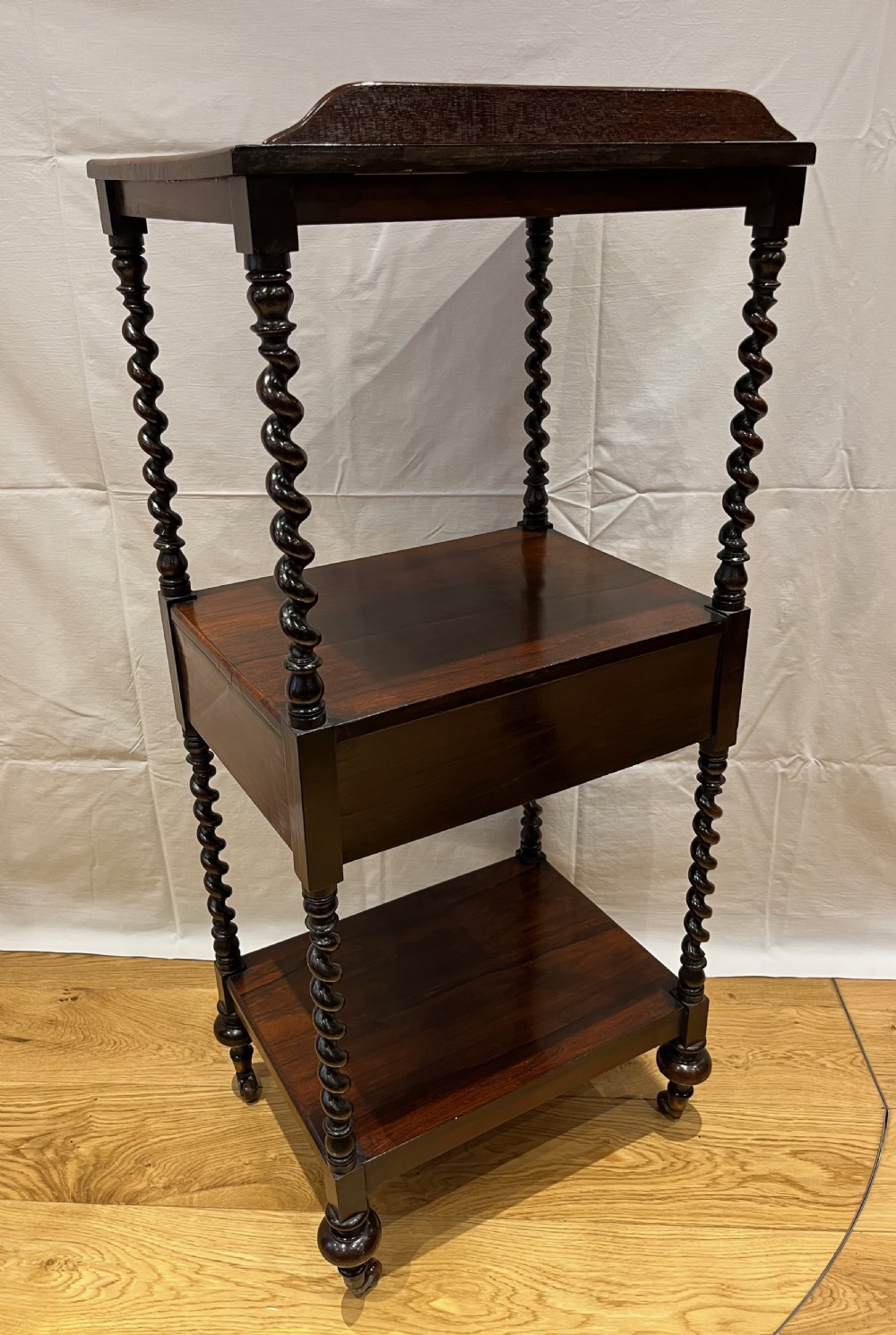 A mid-Victorian dark rosewood whatnot etagere featuring three open tiers, barley twist pillar supports, a central drawer, a gallery back, and turned feet. View IX