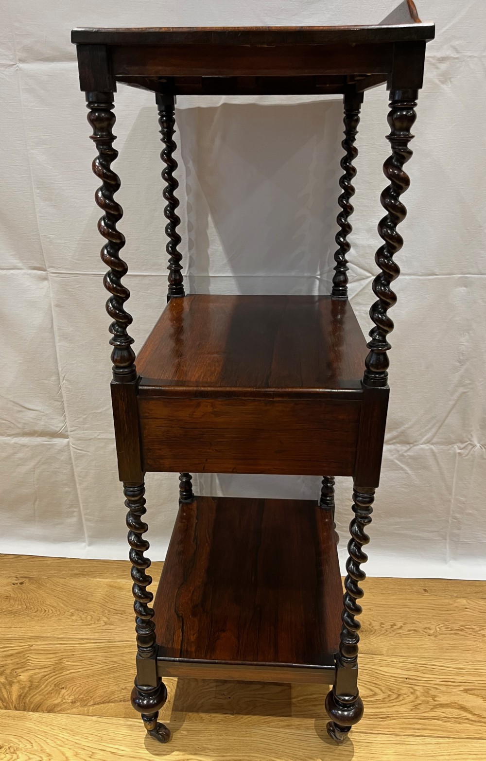 A mid-Victorian dark rosewood whatnot etagere featuring three open tiers, barley twist pillar supports, a central drawer, a gallery back, and turned feet. View X