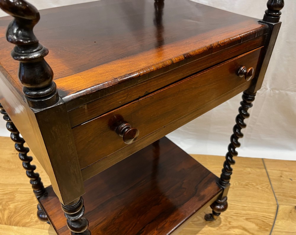 A mid-Victorian dark rosewood whatnot etagere featuring three open tiers, barley twist pillar supports, a central drawer, a gallery back, and turned feet. View XII