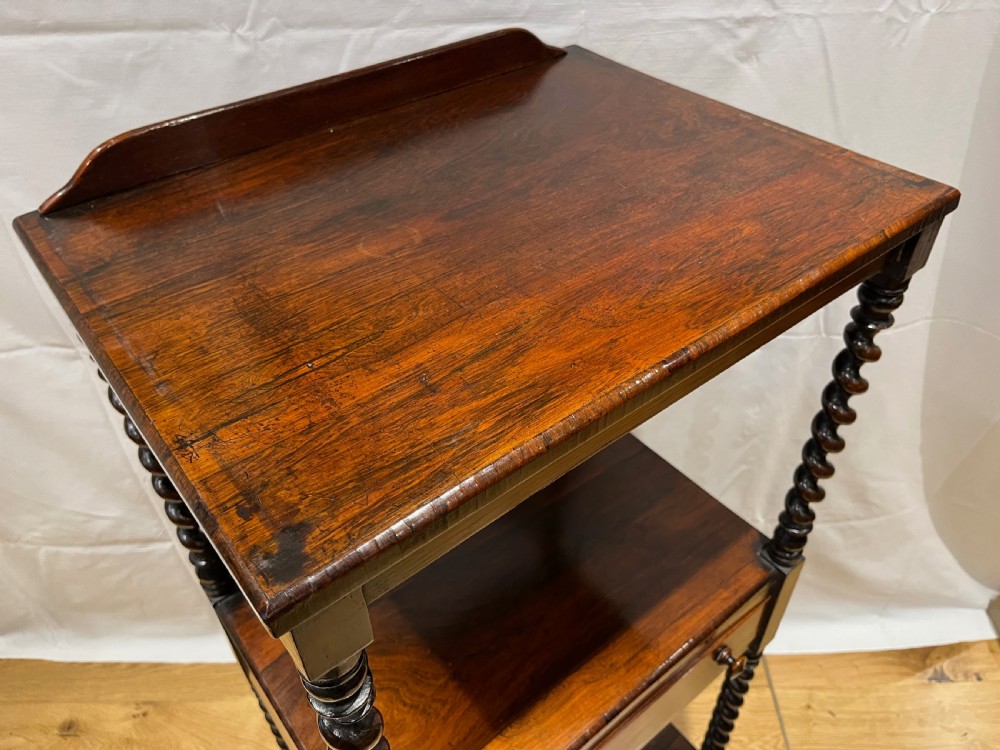 A mid-Victorian dark rosewood whatnot etagere featuring three open tiers, barley twist pillar supports, a central drawer, a gallery back, and turned feet. View XIII