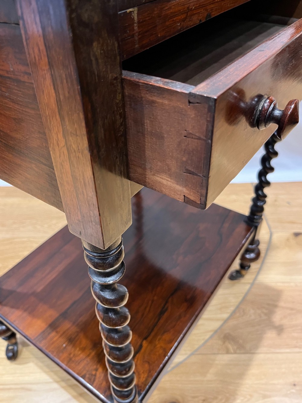 A mid-Victorian dark rosewood whatnot etagere featuring three open tiers, barley twist pillar supports, a central drawer, a gallery back, and turned feet. View XIV