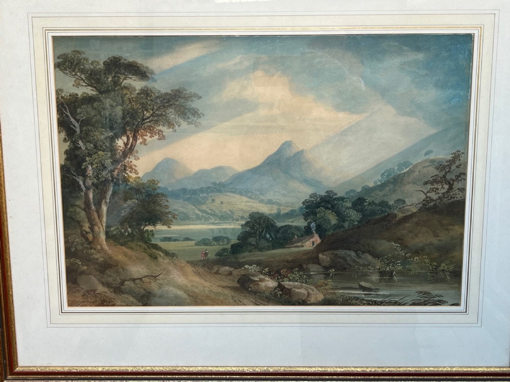 A framed 19th-century watercolour painting featuring a rustic cottage nestled among lush trees with livestock in a rolling landscape, presented in a gilt frame. View X