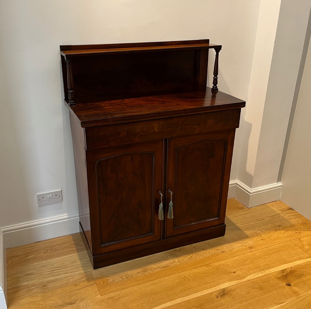 A Regency flame mahogany chiffonier cabinet featuring a top display shelf supported by turned columns over a frieze drawer and two panelled doors. View II