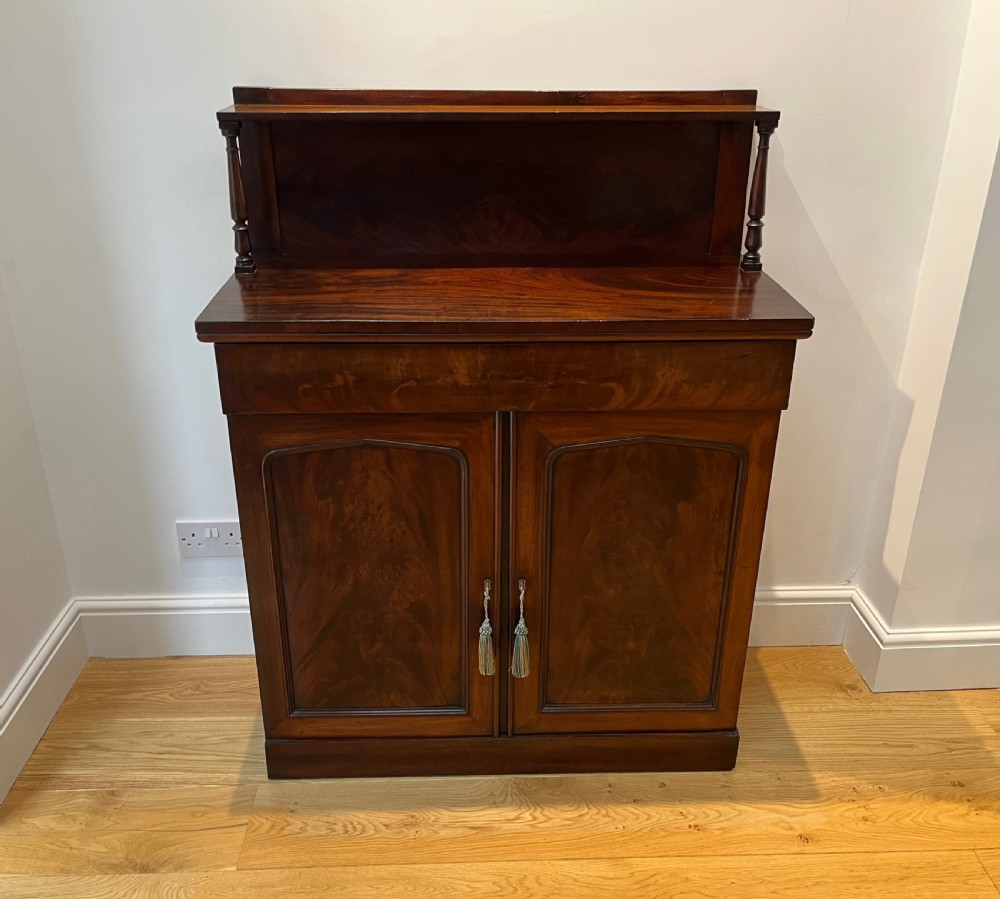 A Regency flame mahogany chiffonier cabinet featuring a top display shelf supported by turned columns over a frieze drawer and two panelled doors. View III