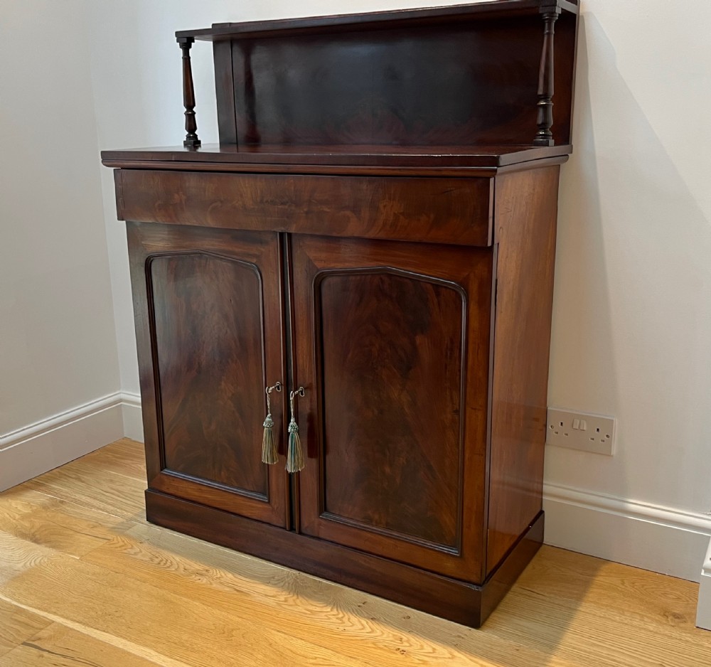 A Regency flame mahogany chiffonier cabinet featuring a top display shelf supported by turned columns over a frieze drawer and two panelled doors. View XI