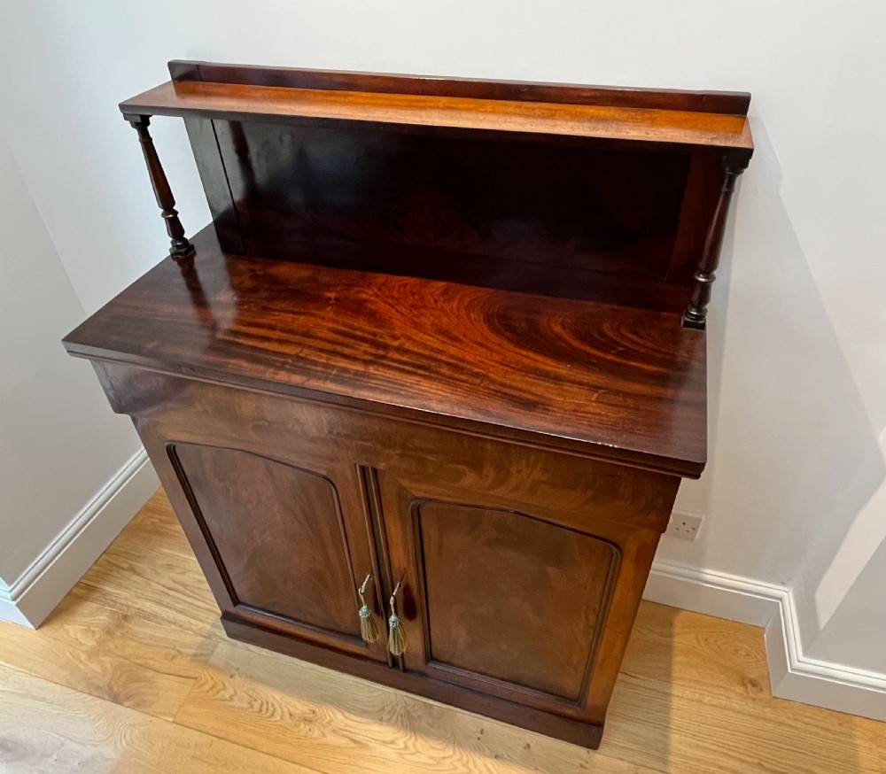A Regency flame mahogany chiffonier cabinet featuring a top display shelf supported by turned columns over a frieze drawer and two panelled doors. View XIV
