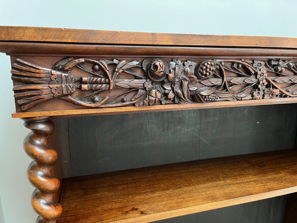 An antique dark walnut open bookcase featuring detailed foliate carved friezes at the top and base flanked by twin barley twist columns framing four shelves. View VI