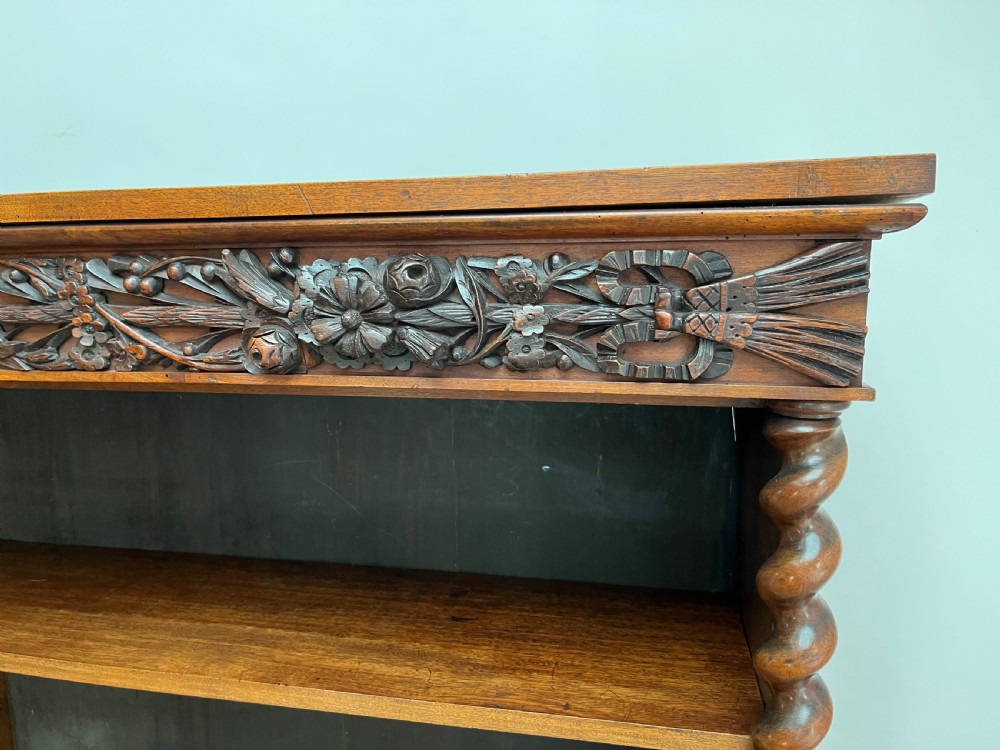 An antique dark walnut open bookcase featuring detailed foliate carved friezes at the top and base flanked by twin barley twist columns framing four shelves. View VII