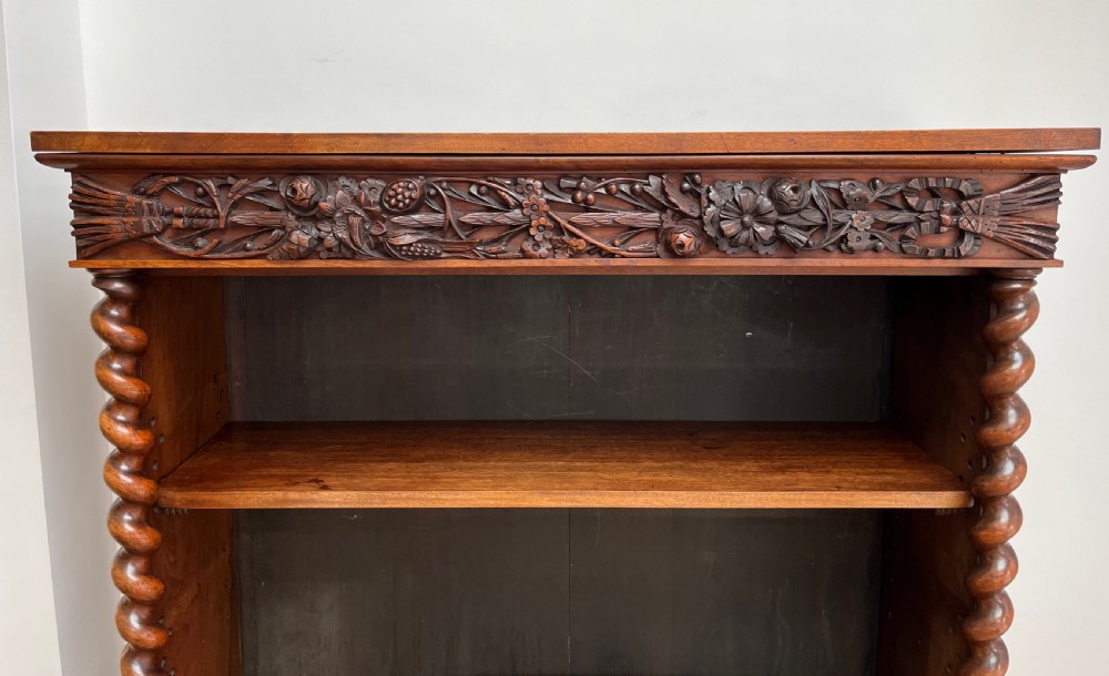 An antique dark walnut open bookcase featuring detailed foliate carved friezes at the top and base flanked by twin barley twist columns framing four shelves. View VIII