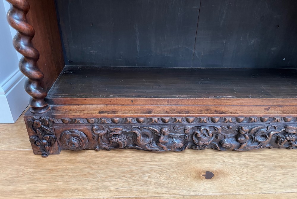 An antique dark walnut open bookcase featuring detailed foliate carved friezes at the top and base flanked by twin barley twist columns framing four shelves. View IX