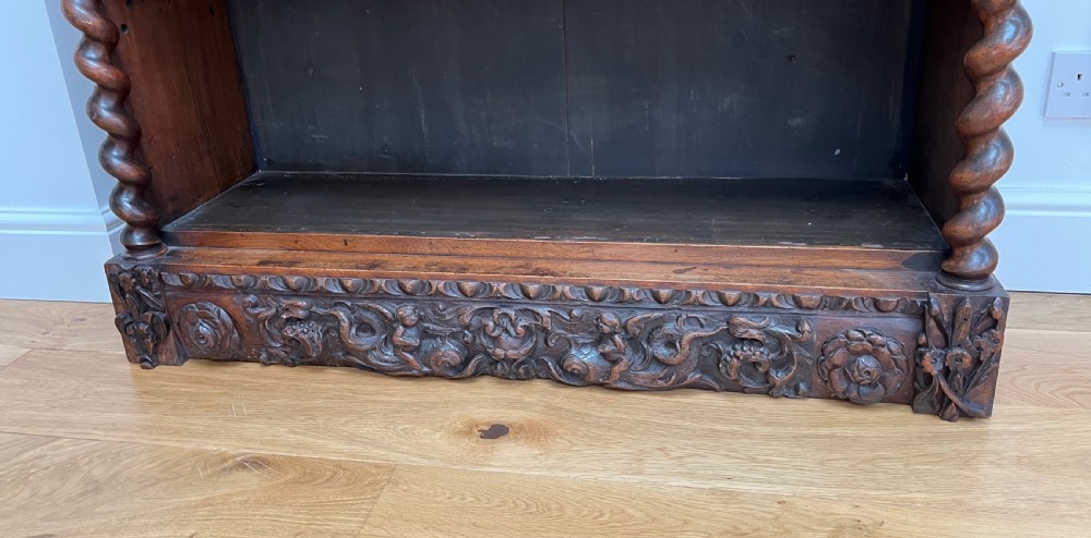 An antique dark walnut open bookcase featuring detailed foliate carved friezes at the top and base flanked by twin barley twist columns framing four shelves. View XI
