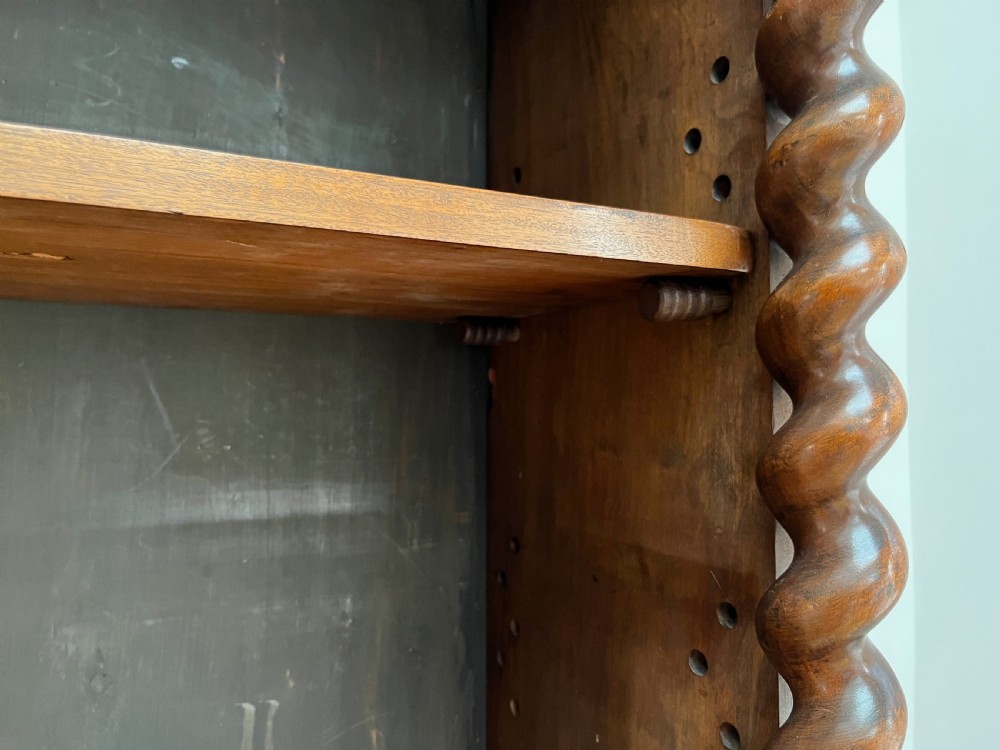 An antique dark walnut open bookcase featuring detailed foliate carved friezes at the top and base flanked by twin barley twist columns framing four shelves. View XII