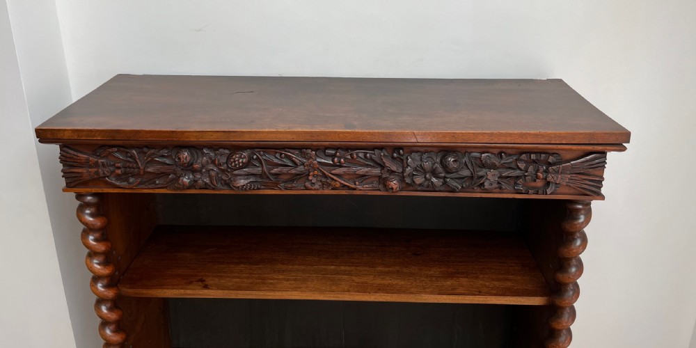 An antique dark walnut open bookcase featuring detailed foliate carved friezes at the top and base flanked by twin barley twist columns framing four shelves. View XV