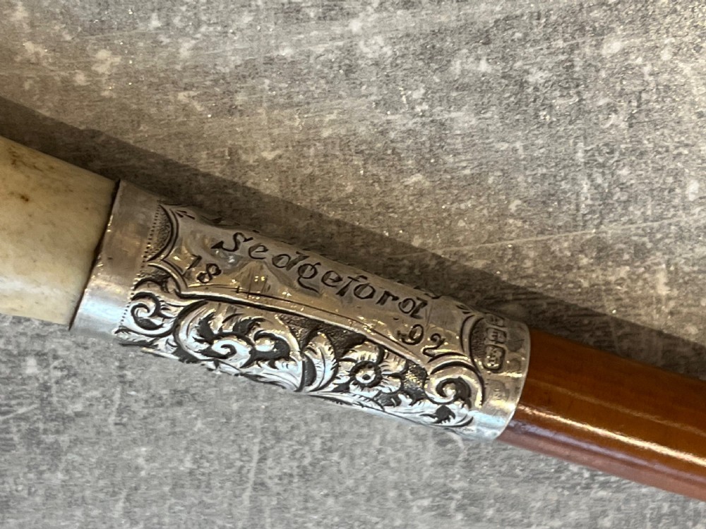 Close-up of a silver-mounted riding crop featuring a carved antler handle, a chased sterling silver collar, and a polished wooden shaft. View IV
