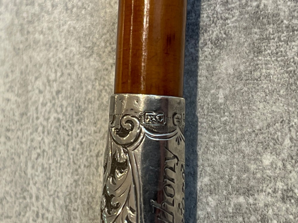 Close-up of a silver-mounted riding crop featuring a carved antler handle, a chased sterling silver collar, and a polished wooden shaft. View V