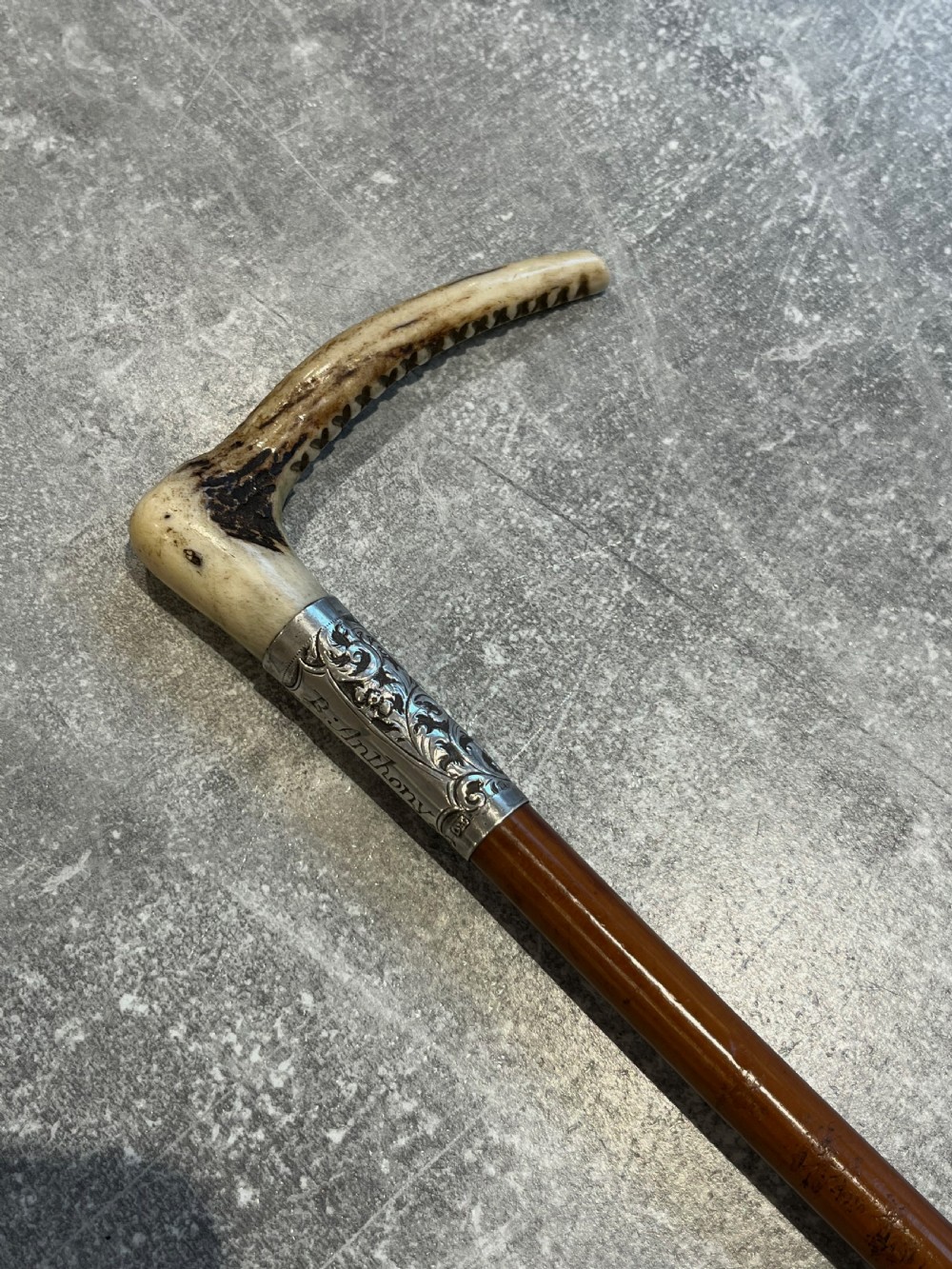 Close-up of a silver-mounted riding crop featuring a carved antler handle, a chased sterling silver collar, and a polished wooden shaft. View VII