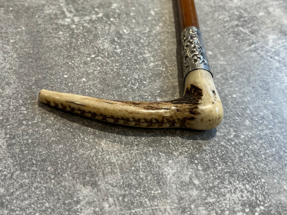 Close-up of a silver-mounted riding crop featuring a carved antler handle, a chased sterling silver collar, and a polished wooden shaft. View IX