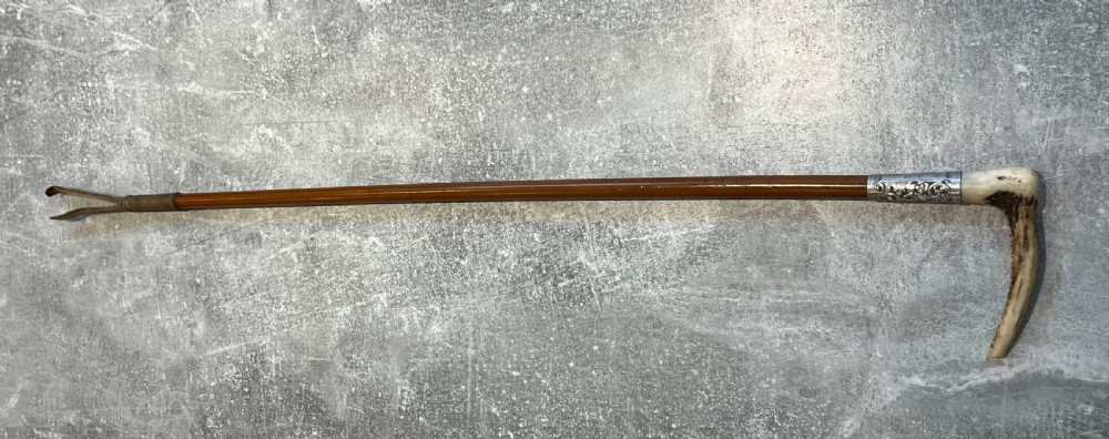 Close-up of a silver-mounted riding crop featuring a carved antler handle, a chased sterling silver collar, and a polished wooden shaft. View X