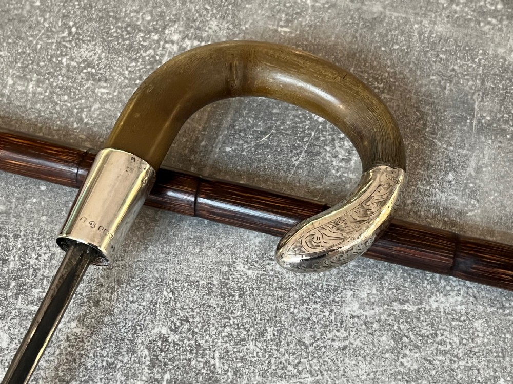 An Edwardian silver-mounted sword stick with a curved crook handle, silver collar bearing London hallmarks, and a partially unsheathed steel blade.