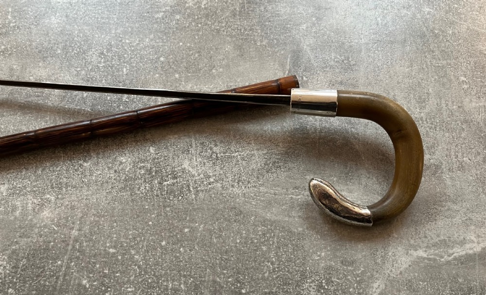 An Edwardian silver-mounted sword stick with a curved crook handle, silver collar bearing London hallmarks, and a partially unsheathed steel blade. View IV