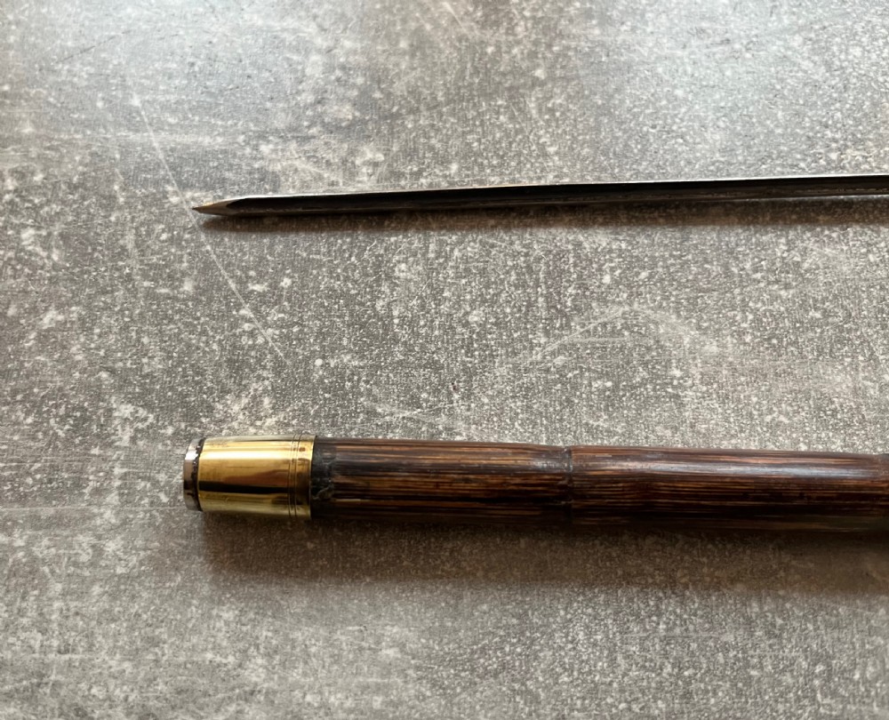 An Edwardian silver-mounted sword stick with a curved crook handle, silver collar bearing London hallmarks, and a partially unsheathed steel blade. View V