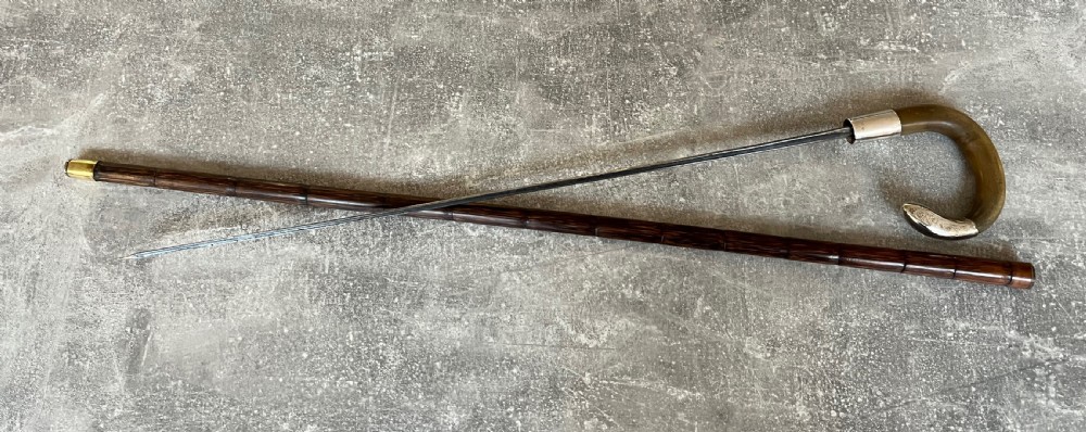 An Edwardian silver-mounted sword stick with a curved crook handle, silver collar bearing London hallmarks, and a partially unsheathed steel blade. View X