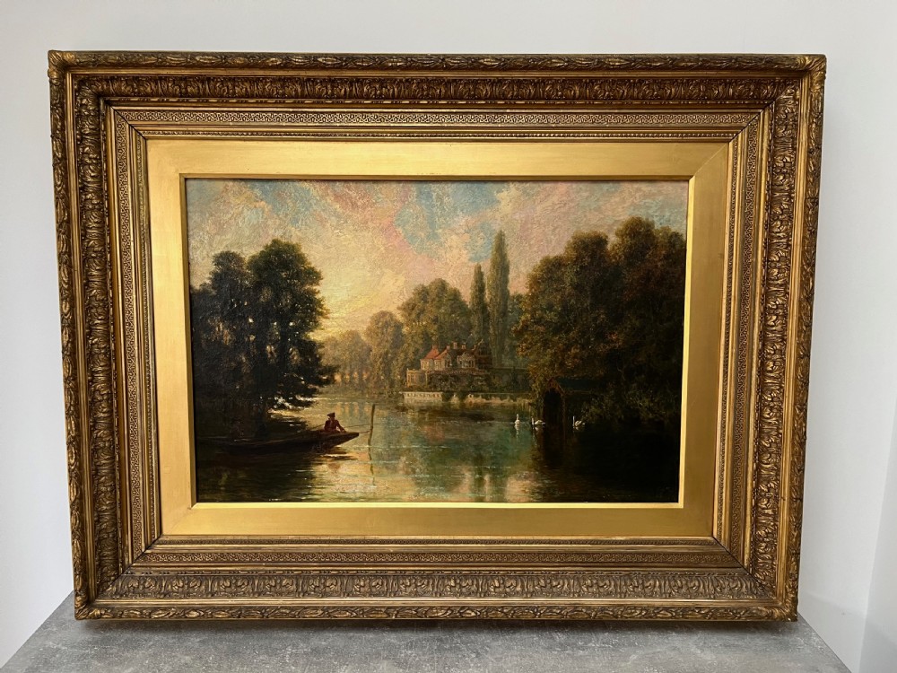An antique framed oil painting depicting a tranquil river Thames scene with a figure in a boat, swans near a boathouse, and a riverbank estate beneath a glowing sky.