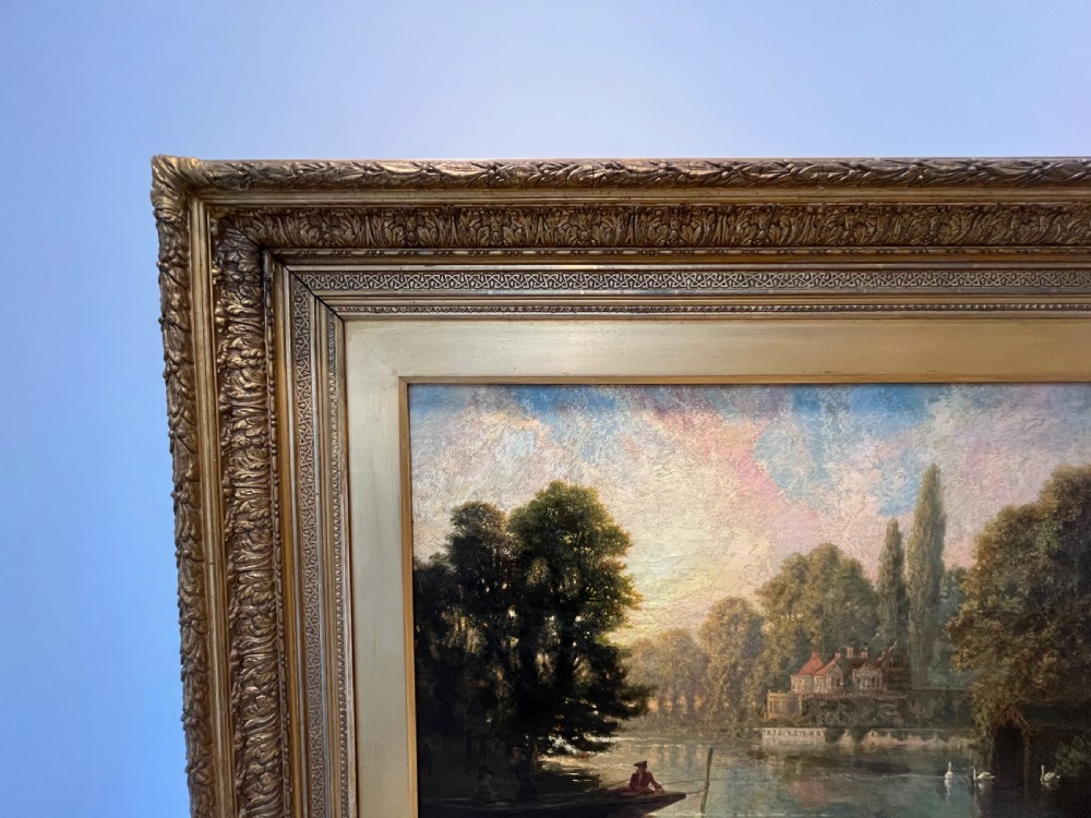An antique framed oil painting depicting a tranquil river Thames scene with a figure in a boat, swans near a boathouse, and a riverbank estate beneath a glowing sky. View VII