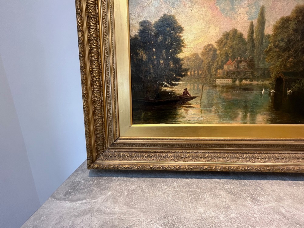 An antique framed oil painting depicting a tranquil river Thames scene with a figure in a boat, swans near a boathouse, and a riverbank estate beneath a glowing sky. View XI