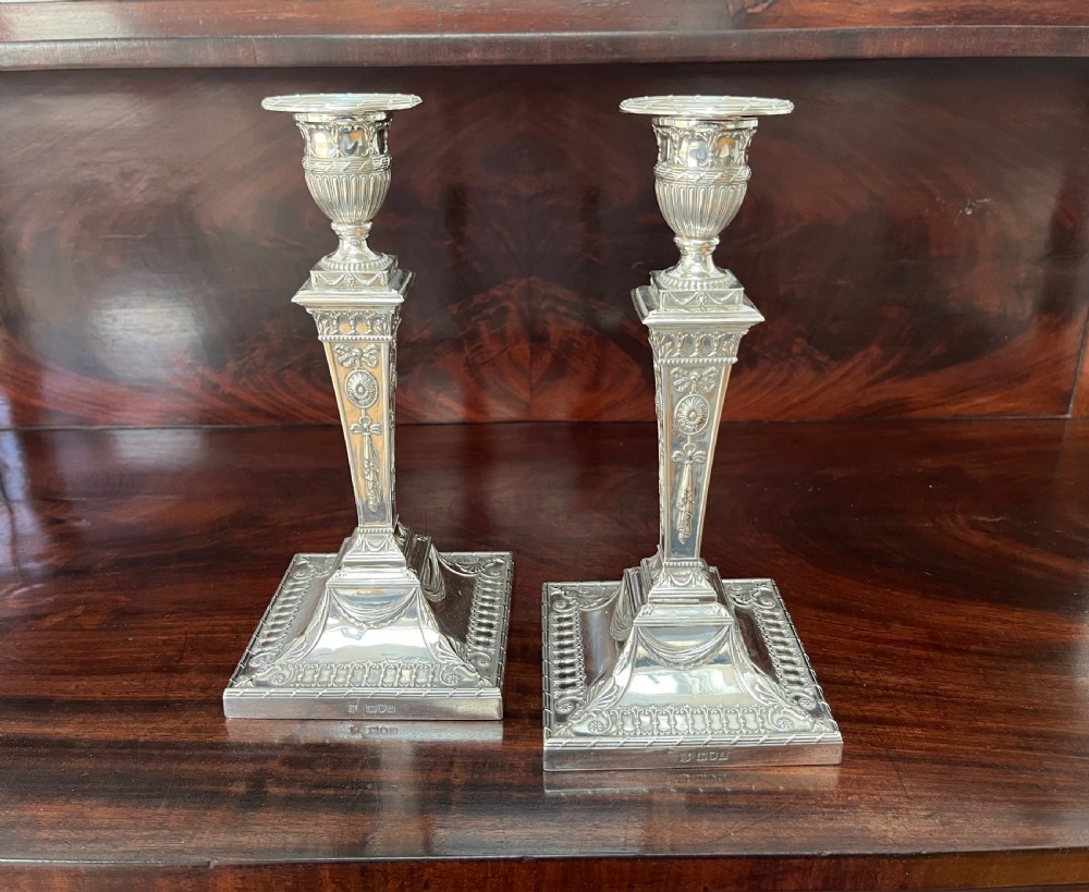 A pair of Victorian sterling silver candlesticks featuring urn-shaped sockets, relief swags on square stepped bases, and tapering columns.