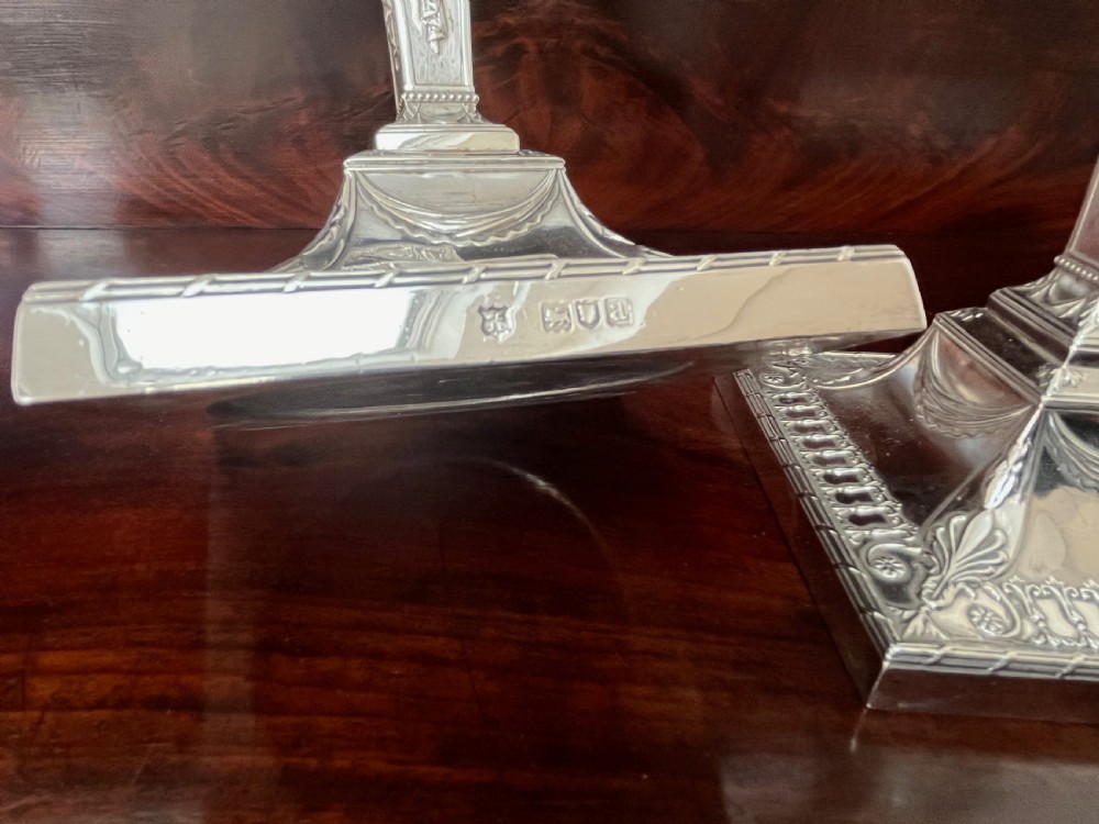 A pair of Victorian sterling silver candlesticks featuring urn-shaped sockets, relief swags on square stepped bases, and tapering columns. View III