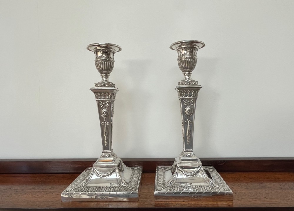 A pair of Victorian sterling silver candlesticks featuring urn-shaped sockets, relief swags on square stepped bases, and tapering columns. View V