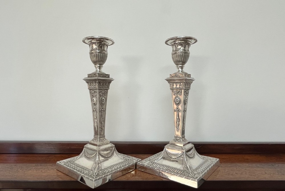 A pair of Victorian sterling silver candlesticks featuring urn-shaped sockets, relief swags on square stepped bases, and tapering columns. View VI