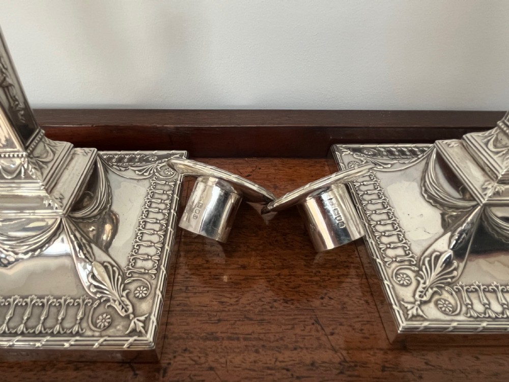 A pair of Victorian sterling silver candlesticks featuring urn-shaped sockets, relief swags on square stepped bases, and tapering columns. View VII