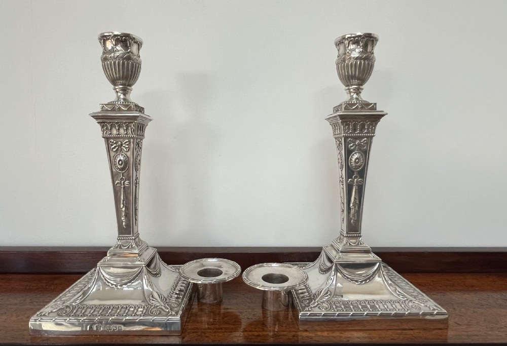 A pair of Victorian sterling silver candlesticks featuring urn-shaped sockets, relief swags on square stepped bases, and tapering columns. View VIII