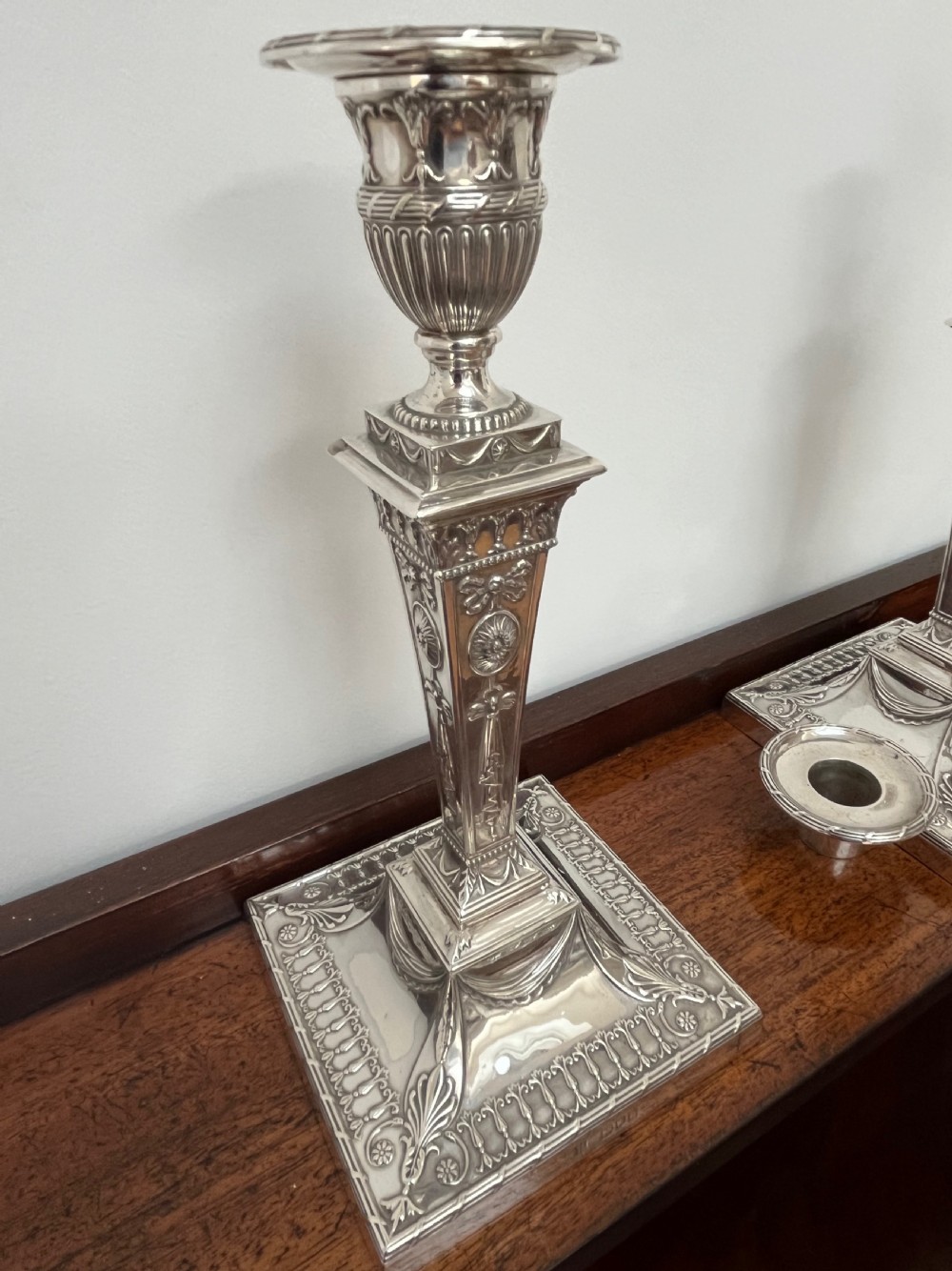 A pair of Victorian sterling silver candlesticks featuring urn-shaped sockets, relief swags on square stepped bases, and tapering columns. View IX
