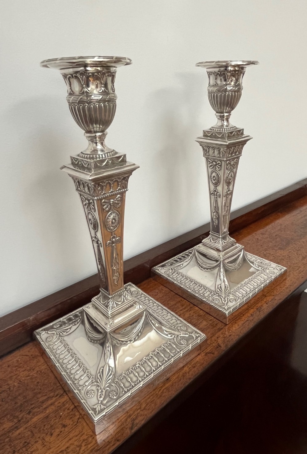 A pair of Victorian sterling silver candlesticks featuring urn-shaped sockets, relief swags on square stepped bases, and tapering columns. View XI