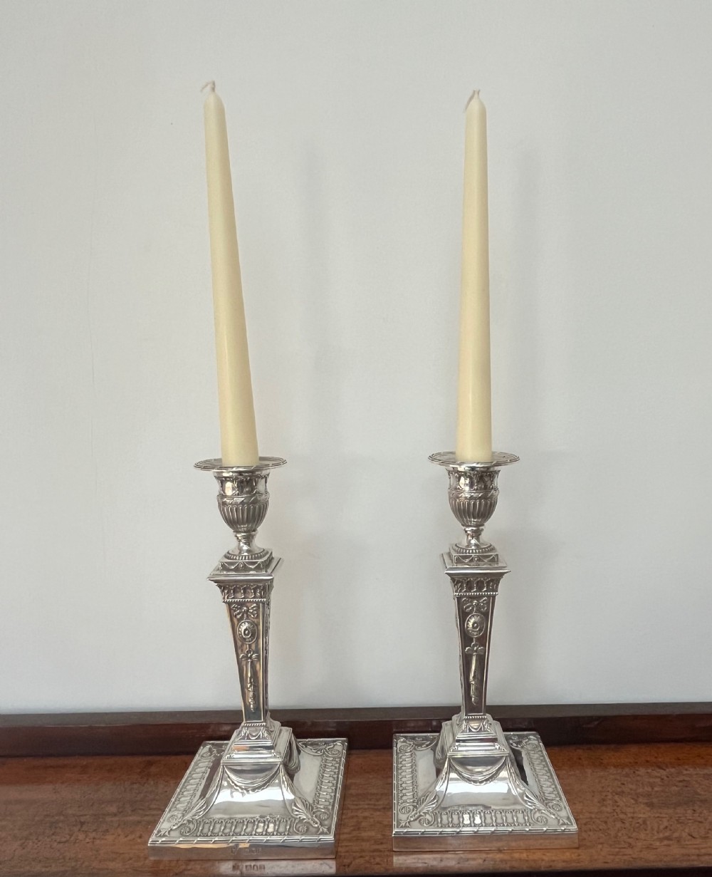 A pair of Victorian sterling silver candlesticks featuring urn-shaped sockets, relief swags on square stepped bases, and tapering columns. View XII