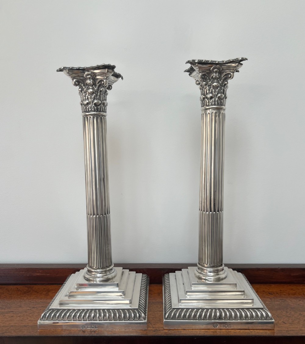 A pair of Edwardian sterling silver Corinthian column candlesticks on stepped square bases with gadrooned rims.