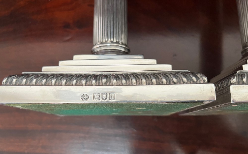 A pair of Edwardian sterling silver Corinthian column candlesticks on stepped square bases with gadrooned rims. View V