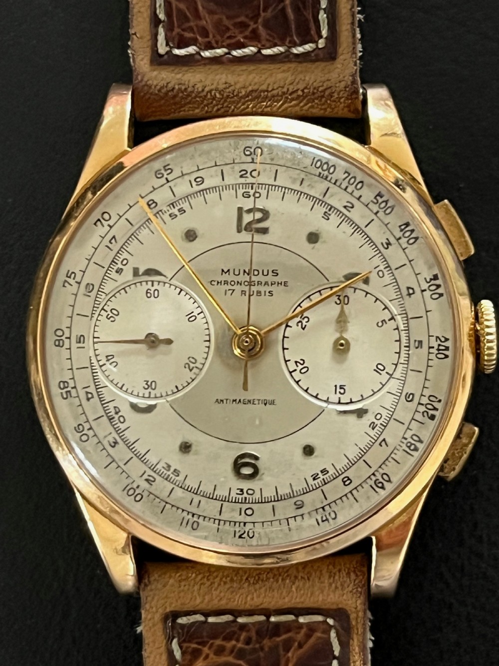 A vintage 18ct gold circular chronograph wristwatch featuring a silvered dial, dual sub-dials, gold hands, and a brown leather strap.