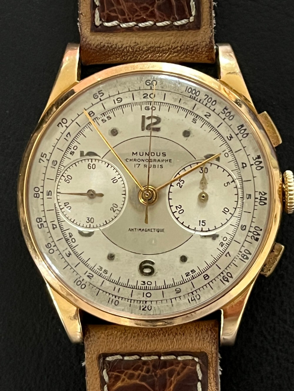 A vintage 18ct gold circular chronograph wristwatch featuring a silvered dial, dual sub-dials, gold hands, and a brown leather strap. View VII