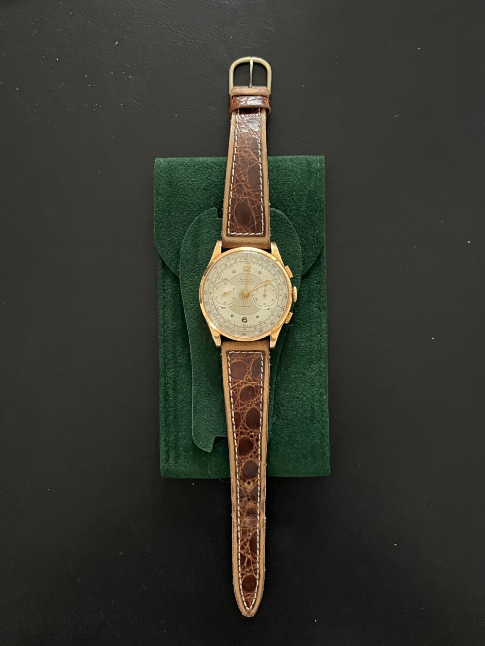 A vintage 18ct gold circular chronograph wristwatch featuring a silvered dial, dual sub-dials, gold hands, and a brown leather strap. View XII