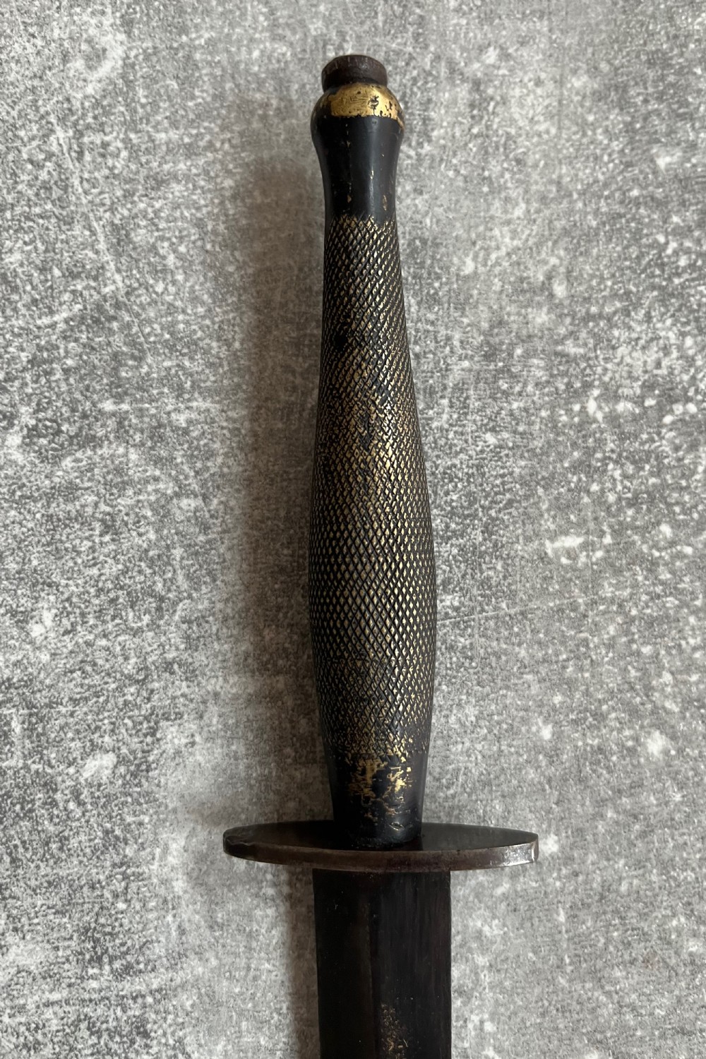 A Second World War Pattern 2 Fairbairn-Sykes combat dagger with a knurled grip resting next to its dark brown leather scabbard. View IV