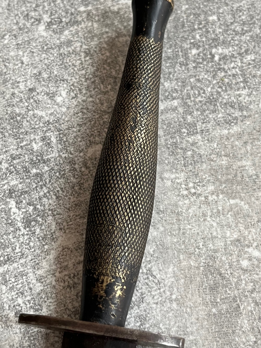 A Second World War Pattern 2 Fairbairn-Sykes combat dagger with a knurled grip resting next to its dark brown leather scabbard. View VIII