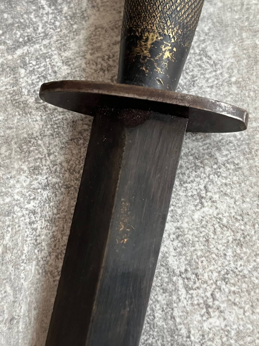 A Second World War Pattern 2 Fairbairn-Sykes combat dagger with a knurled grip resting next to its dark brown leather scabbard. View IX