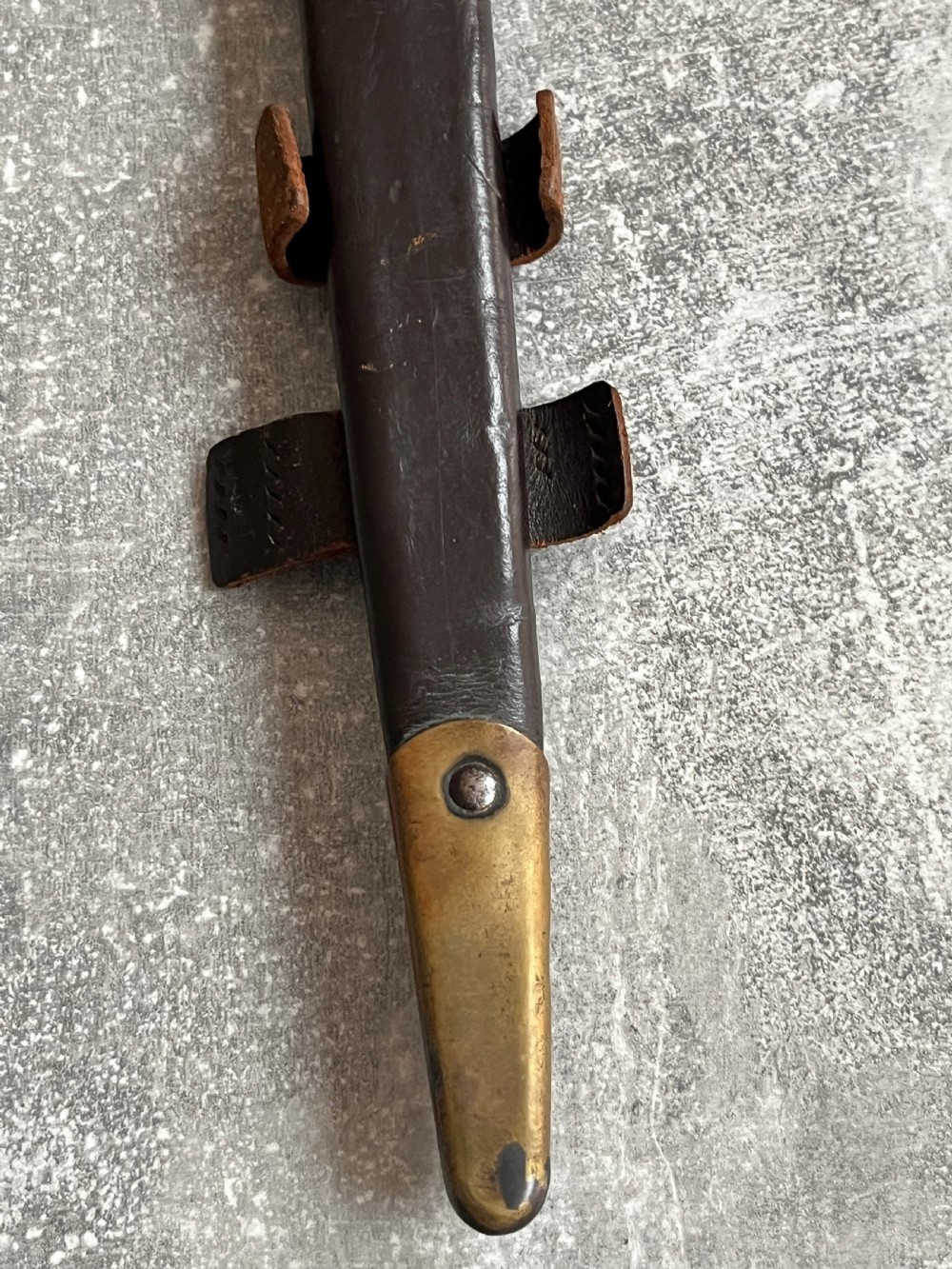 A Second World War Pattern 2 Fairbairn-Sykes combat dagger with a knurled grip resting next to its dark brown leather scabbard. View X