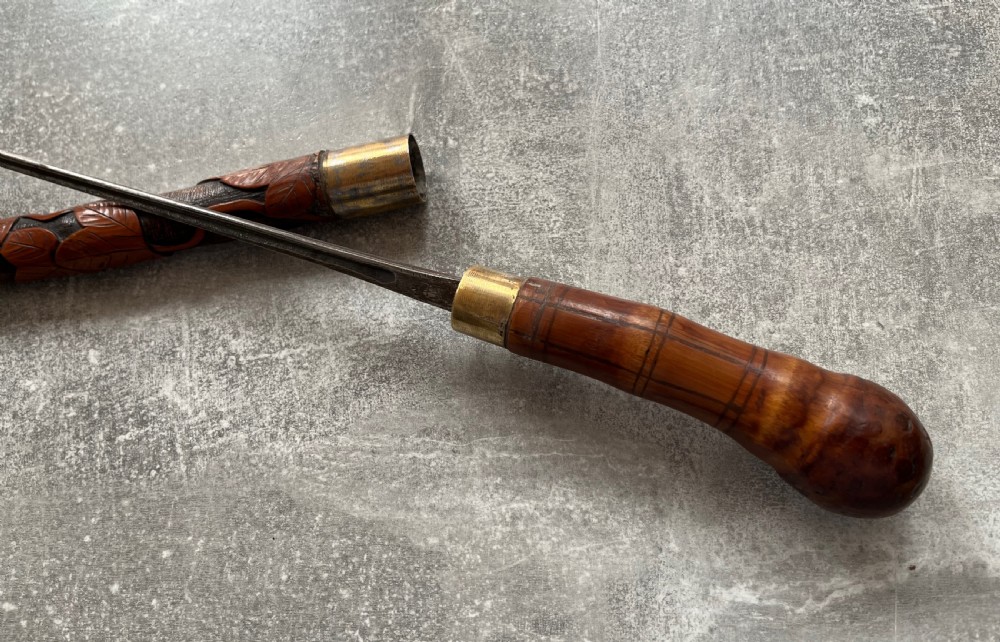 An antique East Asian carved bamboo sword stick shown unsheathed to reveal a long slender steel blade alongside its carved wooden shaft with brass fittings. View III