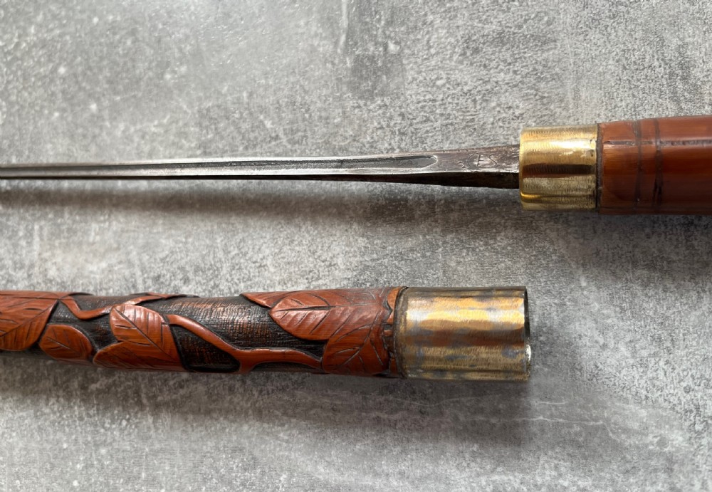 An antique East Asian carved bamboo sword stick shown unsheathed to reveal a long slender steel blade alongside its carved wooden shaft with brass fittings. View IV